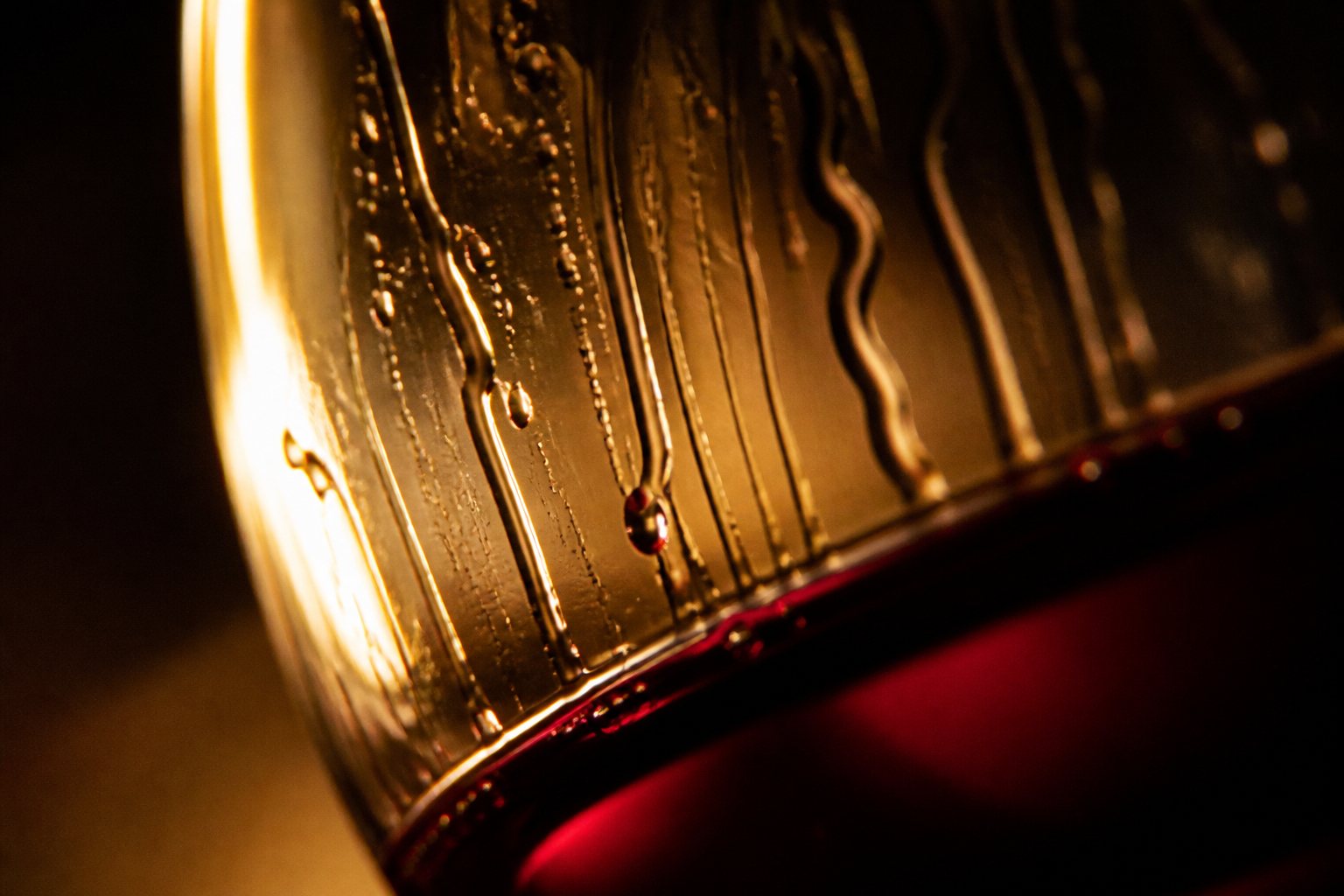 Wine tears running down the inside of a glass, lit gold against the dark